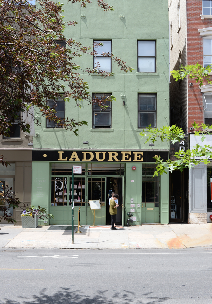 LADUREE 간판이 보이는 녹색 건물 앞에 서 있는 사람의 모습