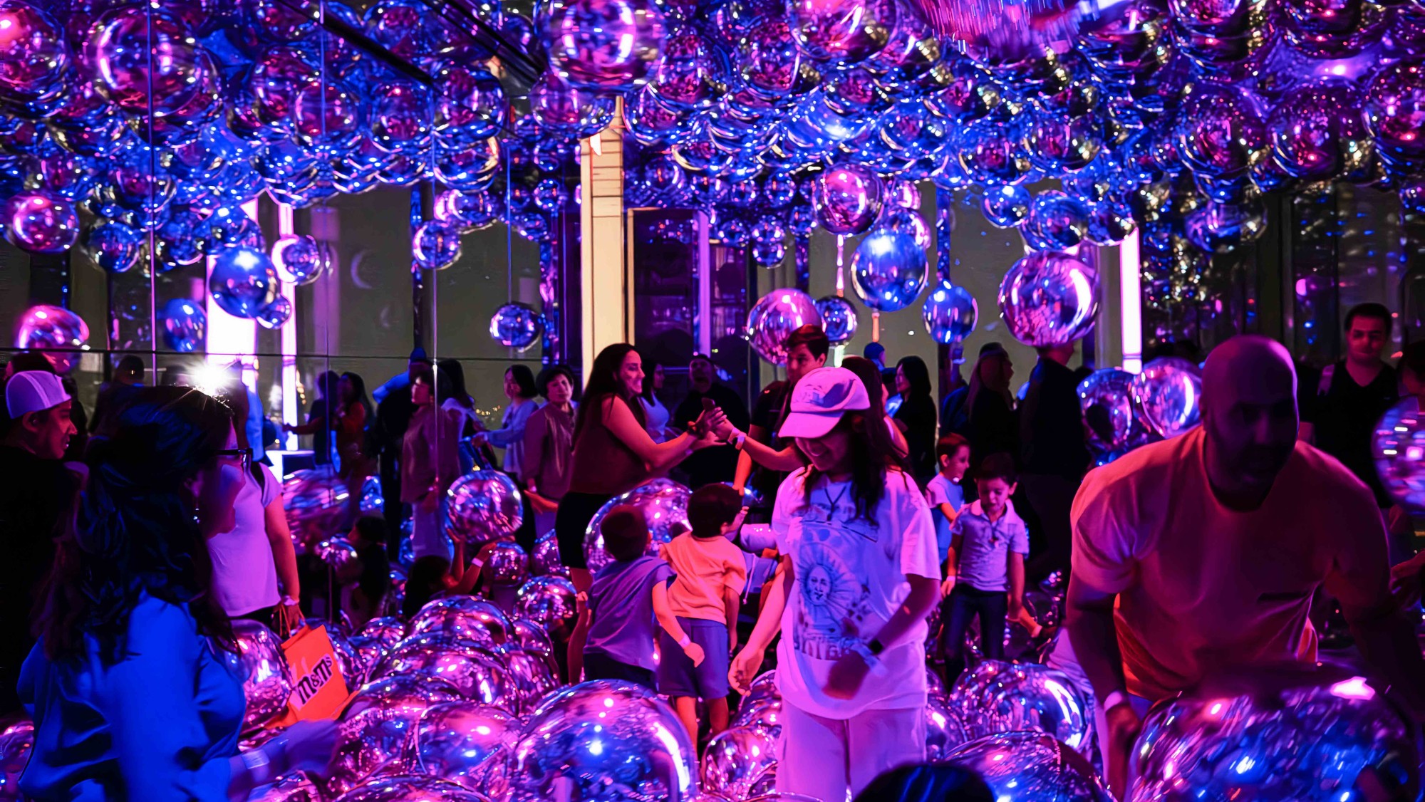 실내 공간에 매달려 있는 반짝이는 구형 장식물과 그 앞에 있는 사람들
