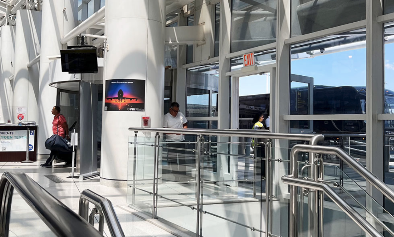 공항 건물 내부에 투명 패널로 된 계단과 유리창이 있는 공간, 사람과 간판이 보입니다