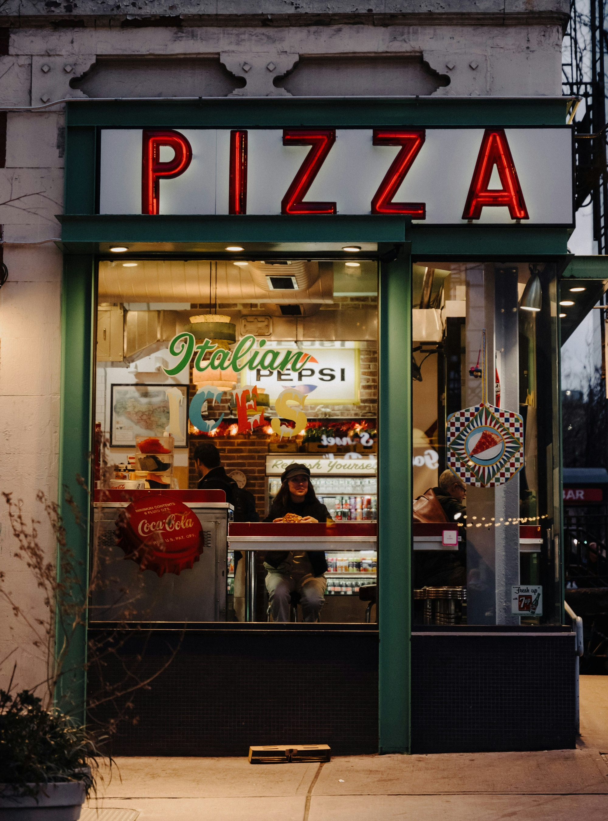 PIZZA라는 문구가 적힌 간판과 유리창이 보이는 도시의 피자 가게 건물 전경