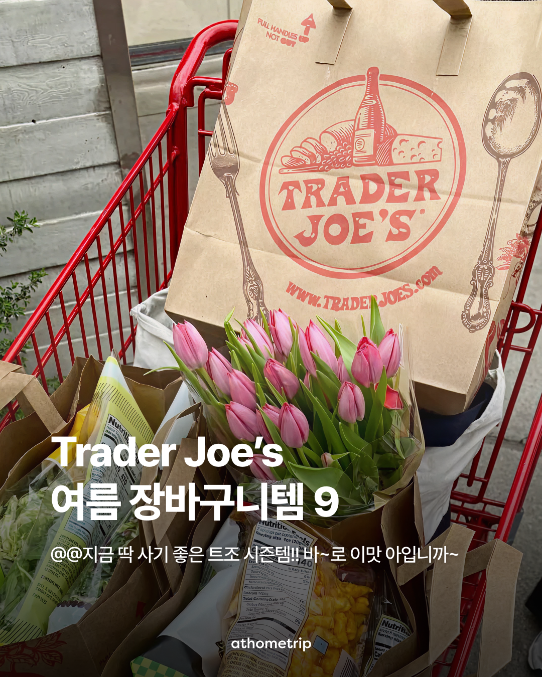 빨간색 쇼핑카트에 트레이더 조이스 로고가 적힌 종이 봉투와 분홍색 튤립 꽃다발, 식품 포장물이 담겨 있는 실외 사진