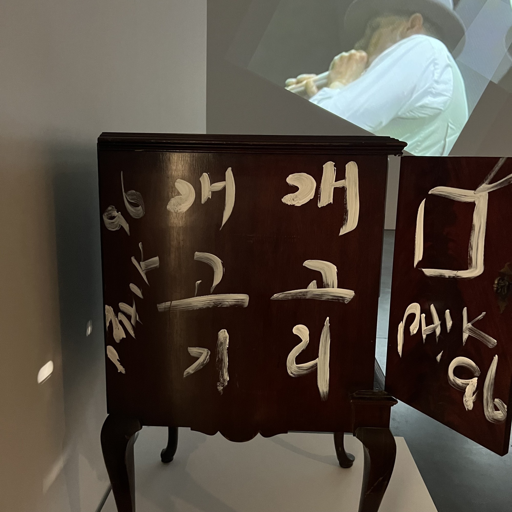 문이 열려 있고 표면에 흰색 글씨가 쓰인 전시 공간 내 목재 서랍장