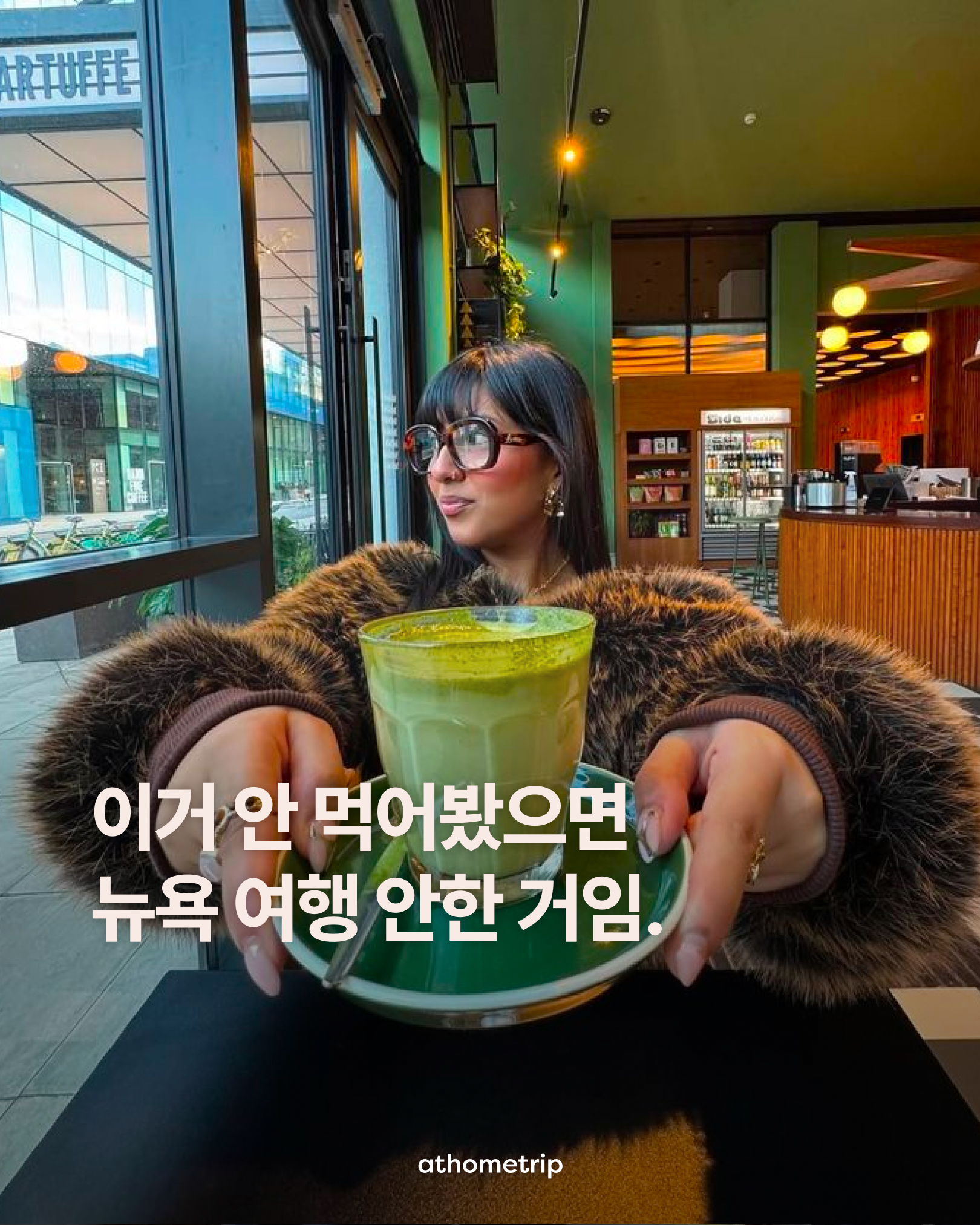 카페 테이블에 앉아 컵과 접시가 놓인 테이블 위에서 녹색 음료를 들고 있는 사람의 모습