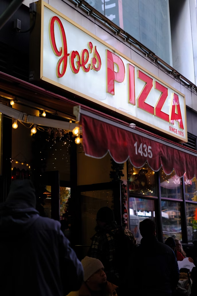 Joe's PIZZA라는 글자가 적힌 간판과 가게 앞에 있는 사람들의 모습