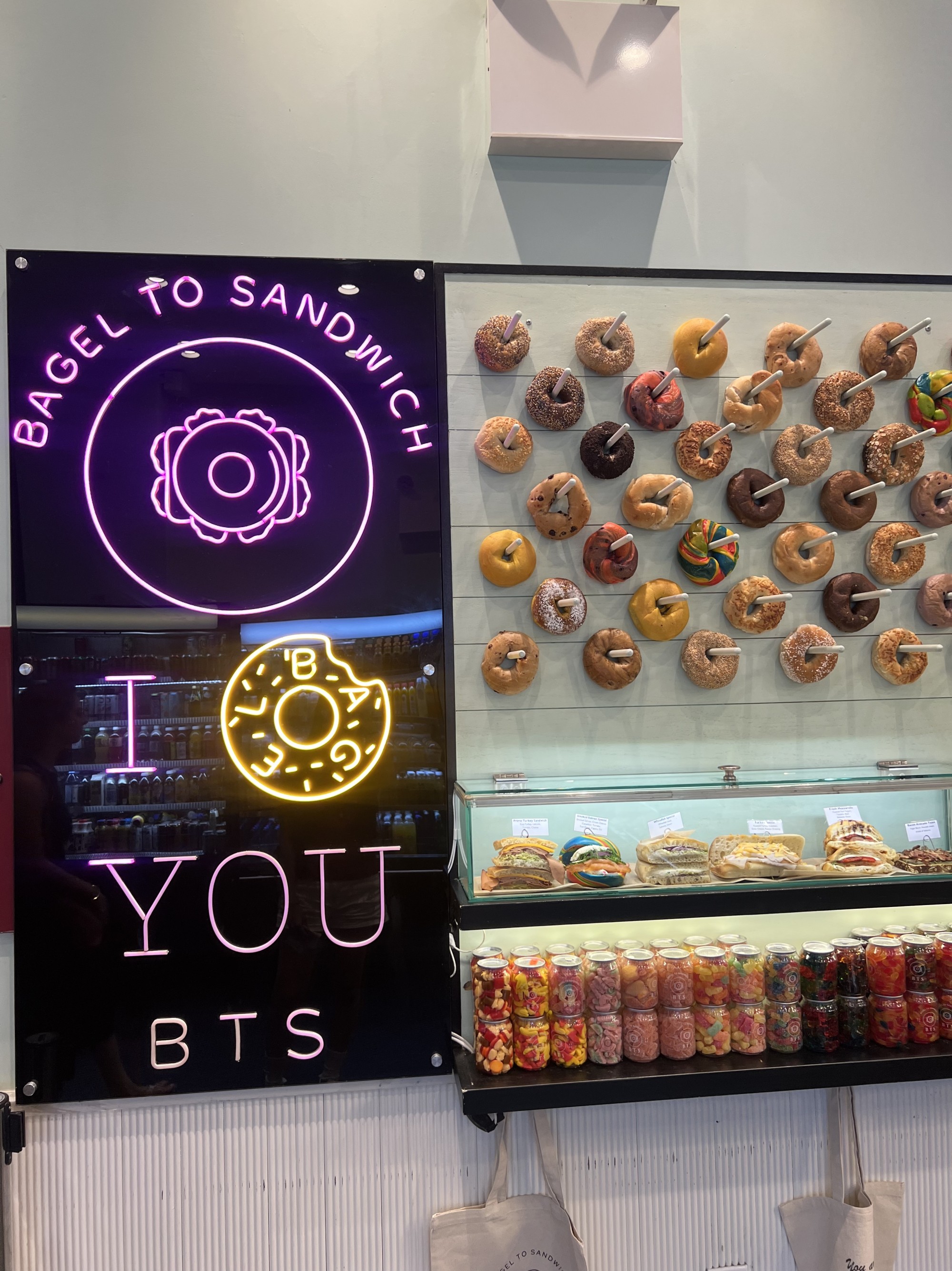 BAGEL TO SANDWICH 문구가 적힌 전광판과 도넛, 캔 음료 등 간식이 진열된 실내 모습