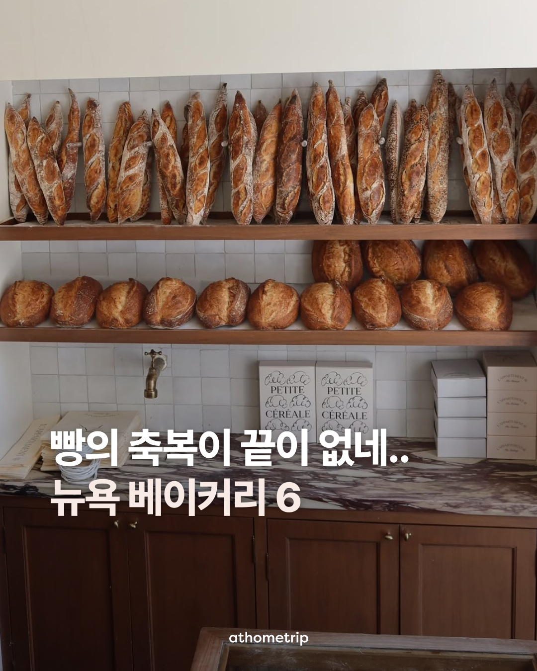 실내에서 여러 종류의 빵이 선반에 진열되어 있으며, 아래쪽에는 나무 캐비닛과 흰색 상자들이 배치된 장면
